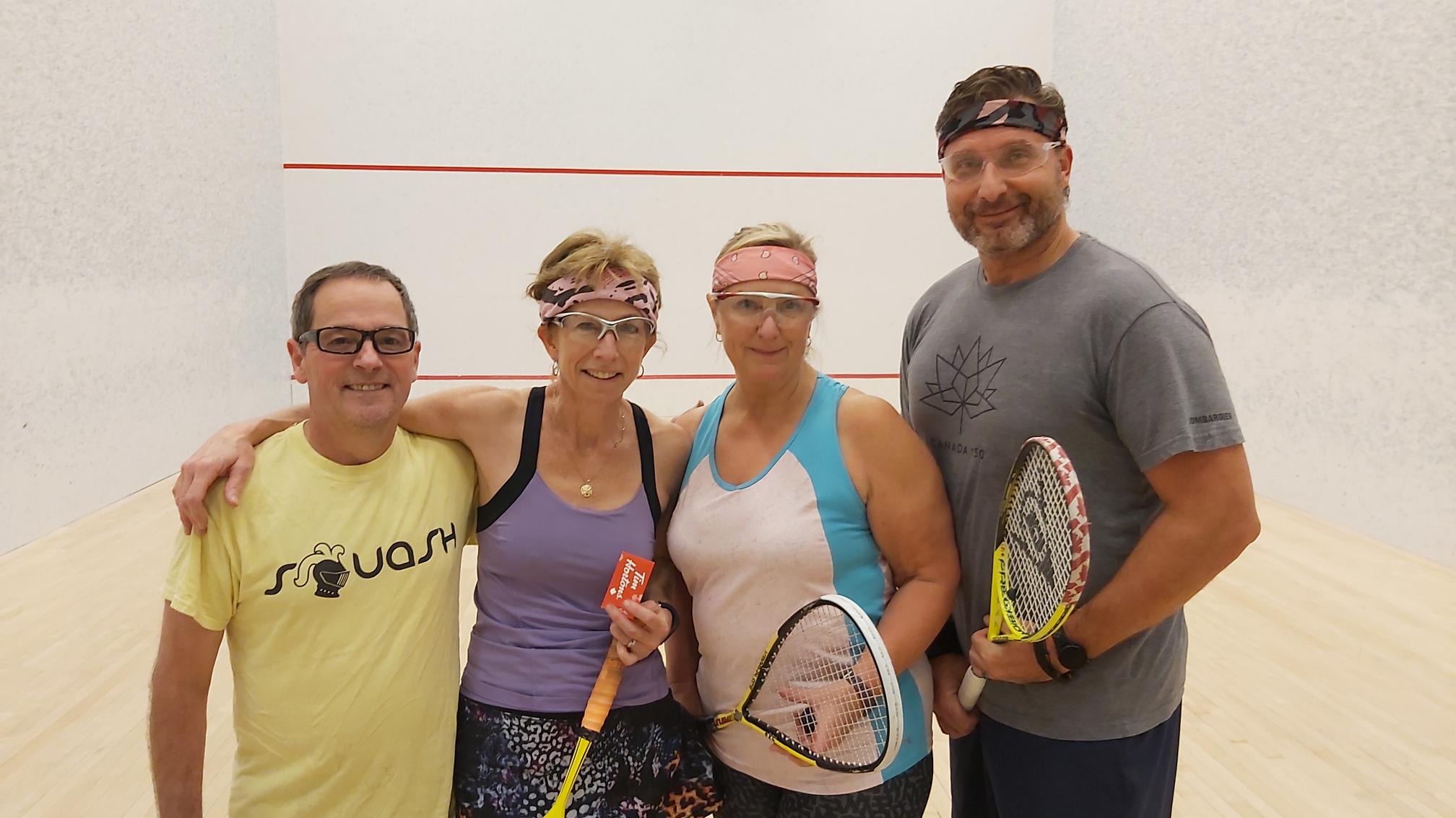 Four friends posing and smiling on a squash court, highlighting the Pickering Squash Club community.